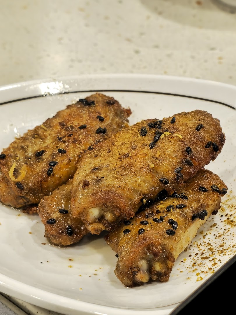 A close-up of four golden-brown seasoned chicken wings with black sesame seeds on a white plate.