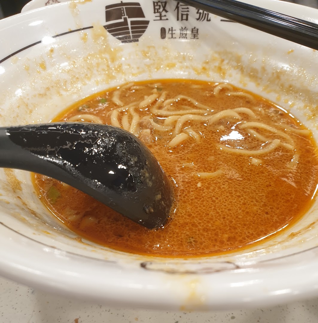 A close-up of a bowl of spicy noodles with a black spoon.