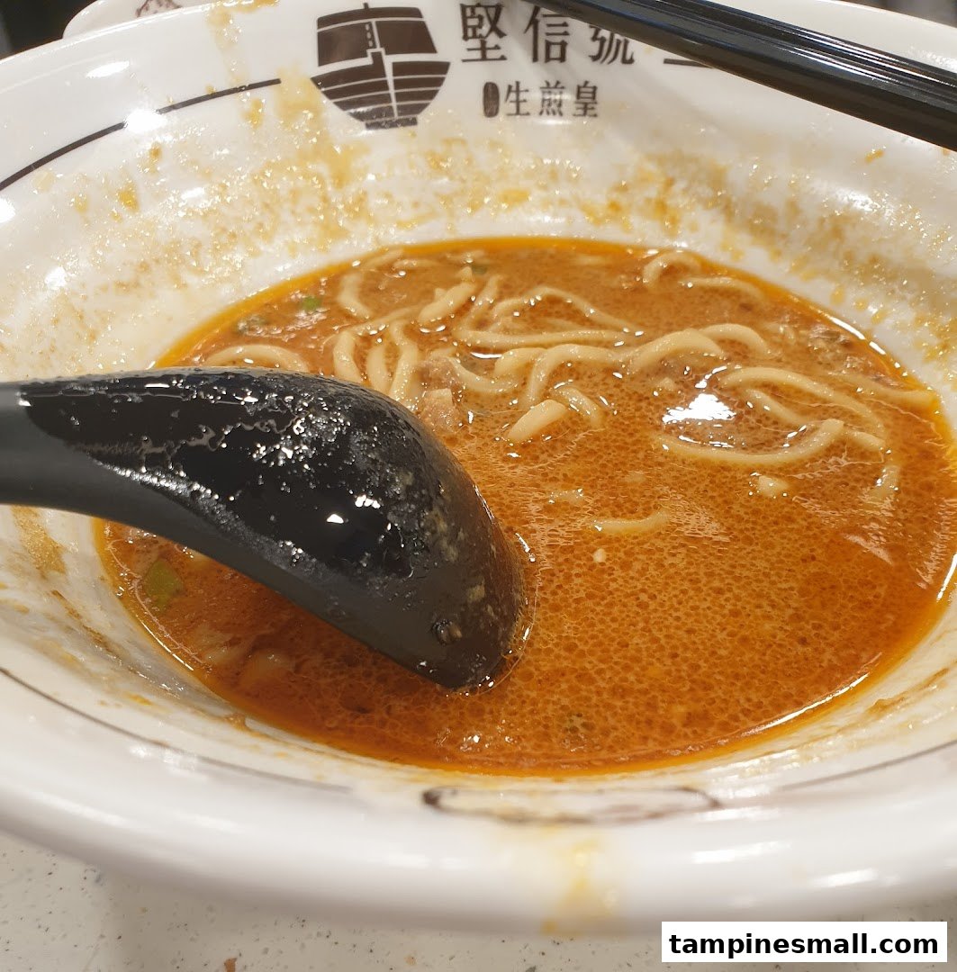 A close-up of a bowl of spicy noodles with a black spoon.