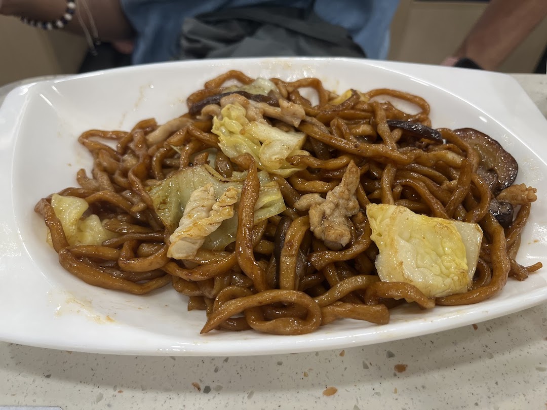 A close-up of a plate of savory stir-fried noodles with pork and cabbage.