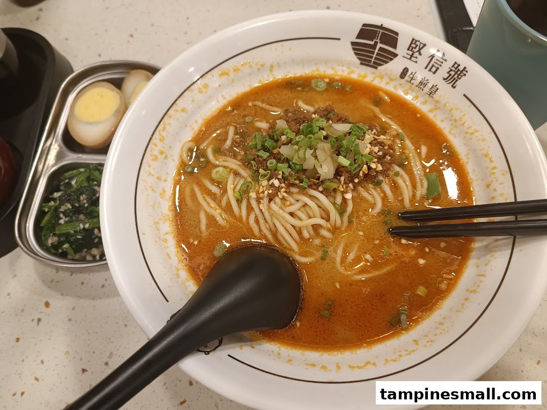 A vibrant bowl of spicy noodles with minced meat and green onions, accompanied by side dishes.