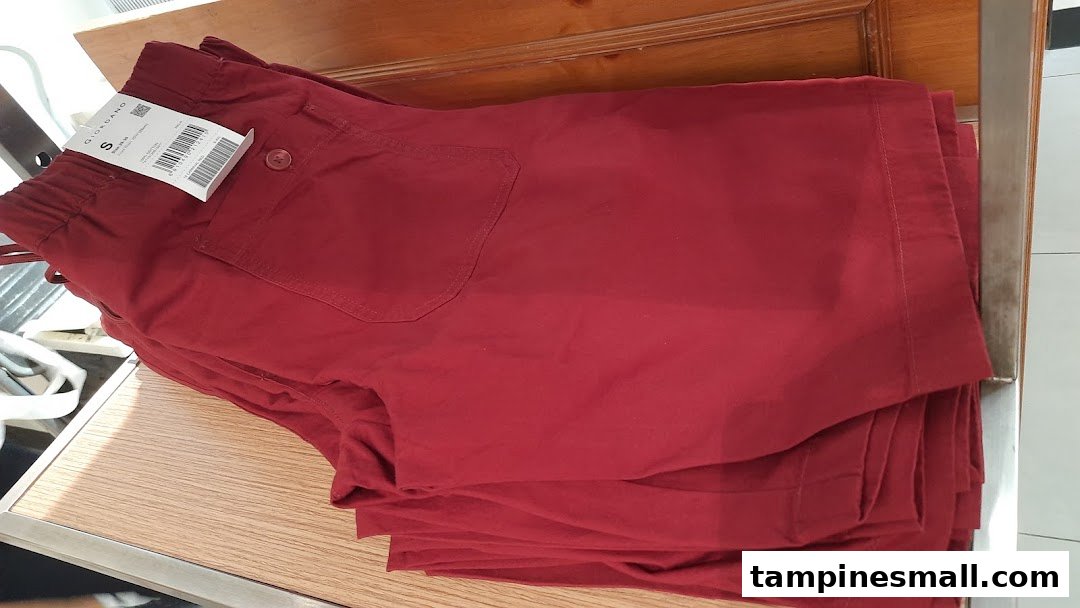 A stack of red casual shorts or pants with a Giordano tag on display in a retail store.