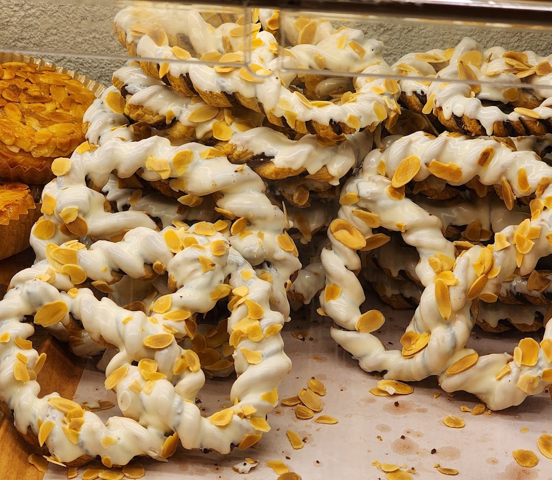 Close-up of ring-shaped pastries with white icing and almond flakes in a bakery display.