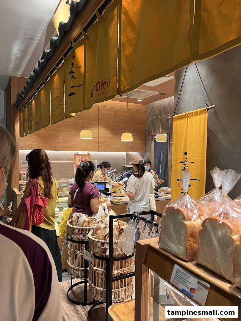 Customers queueing at the counter of a bustling Japanese bakery, with fresh bread on display.