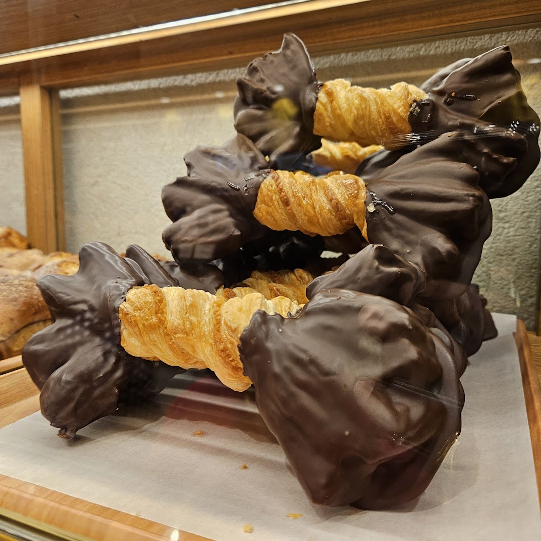 Close-up of chocolate-dipped pastries, possibly croissants, displayed in a bakery case.