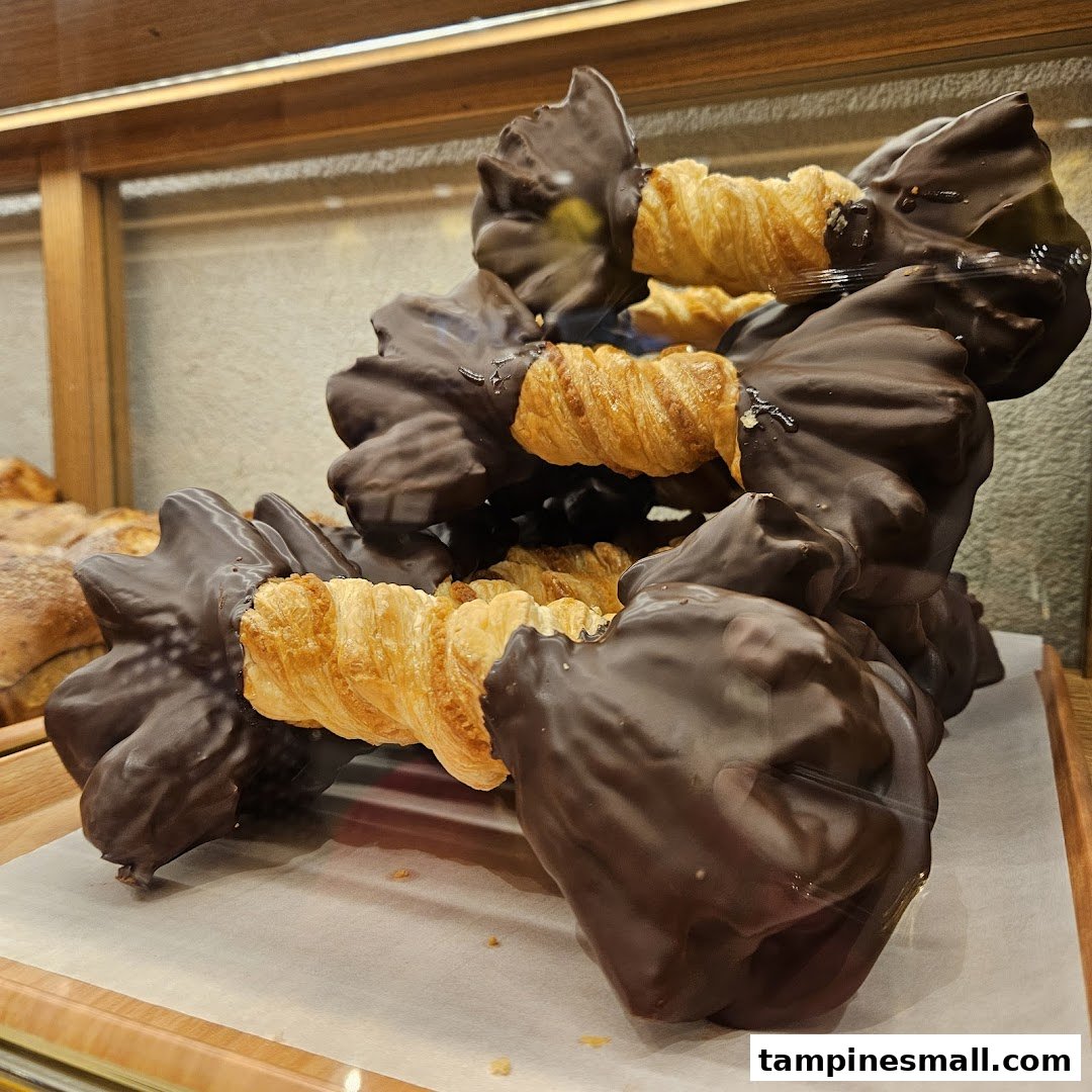 Close-up of chocolate-dipped pastries, possibly croissants, displayed in a bakery case.