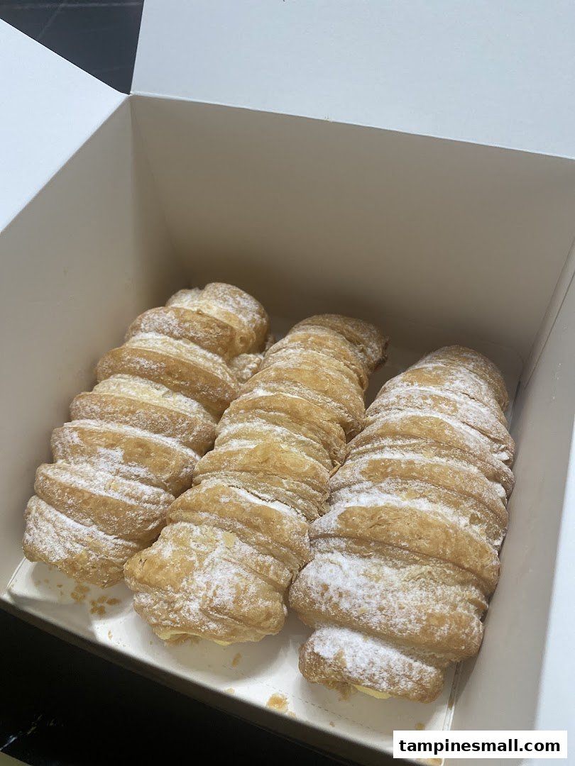 Three golden, flaky pastries dusted with powdered sugar, presented in a white box.
