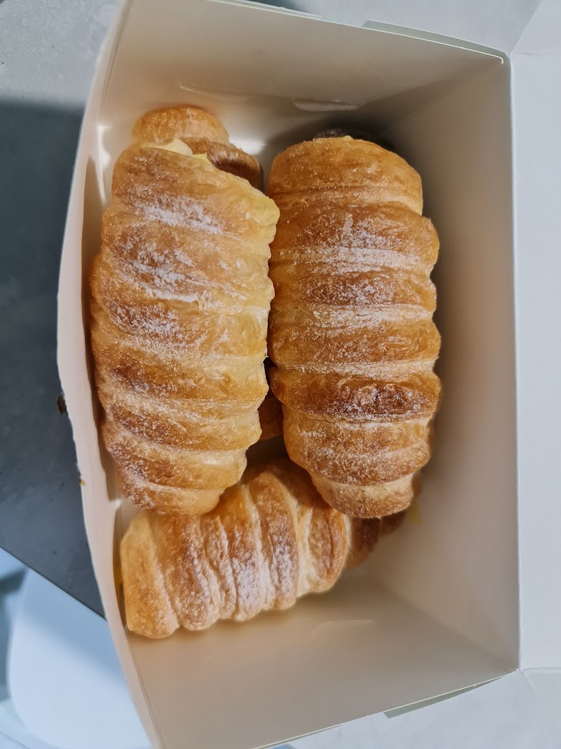 Three golden-brown pastries, possibly cream horns or croissants, dusted with powdered sugar in a white box.