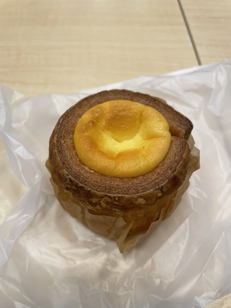 A close-up of a delicious-looking layered pastry with a creamy yellow filling, presented in a paper wrapper.