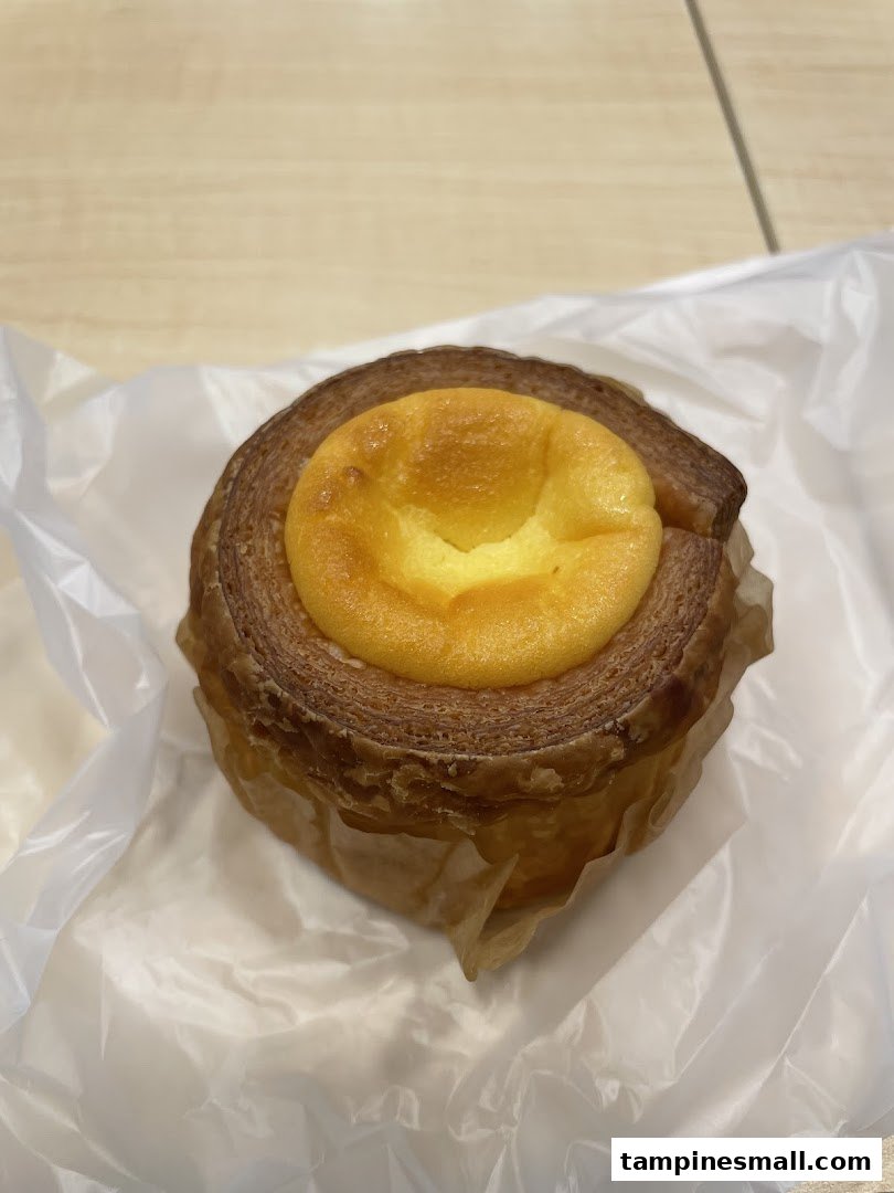 A close-up of a delicious-looking layered pastry with a creamy yellow filling, presented in a paper wrapper.
