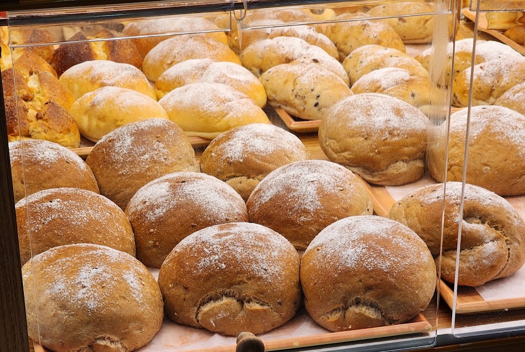 A display case filled with various freshly baked bread rolls, some dusted with powdered sugar.