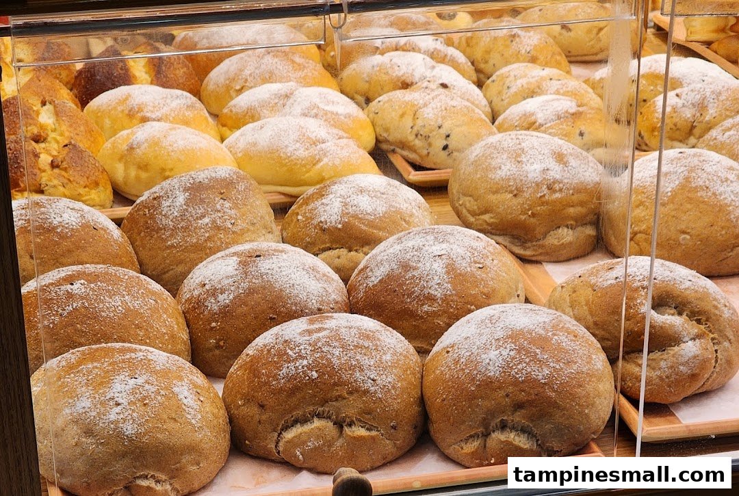 A display case filled with various freshly baked bread rolls, some dusted with powdered sugar.