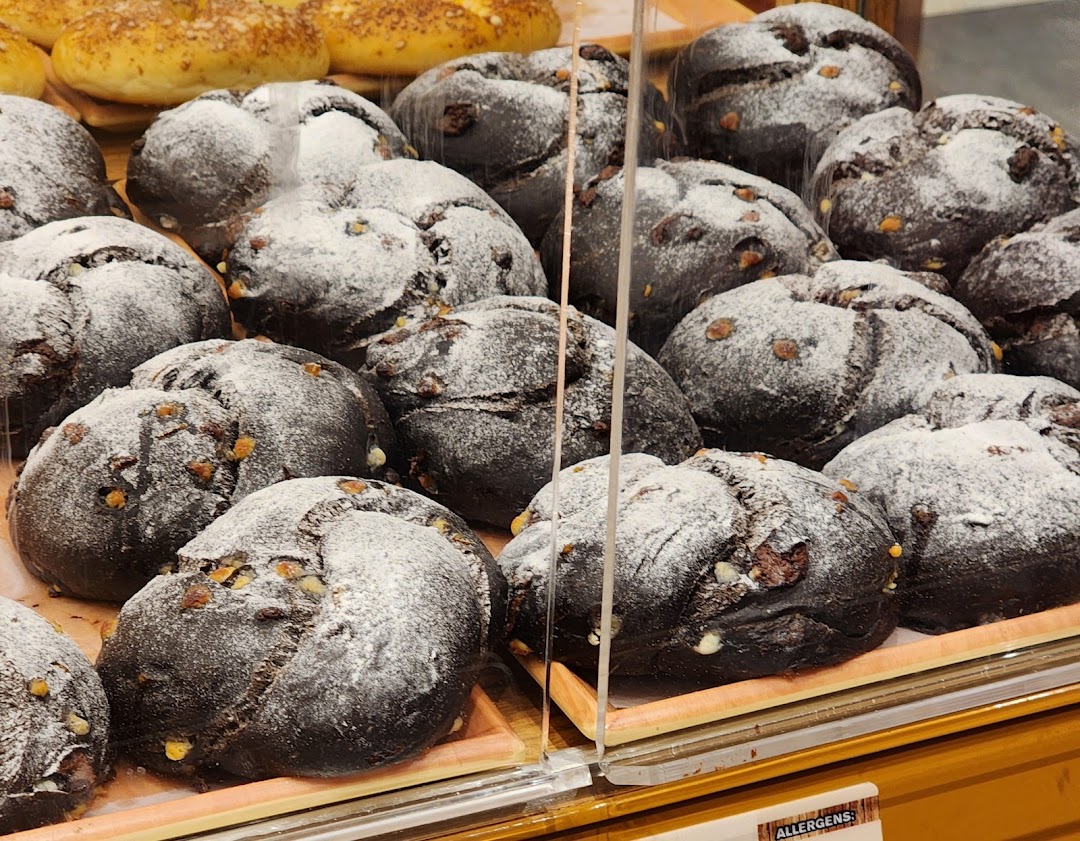 Close-up of dark, round loaves of bread dusted with powdered sugar and nuts, displayed in a bakery case.