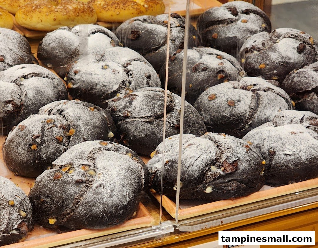 Close-up of dark, round loaves of bread dusted with powdered sugar and nuts, displayed in a bakery case.