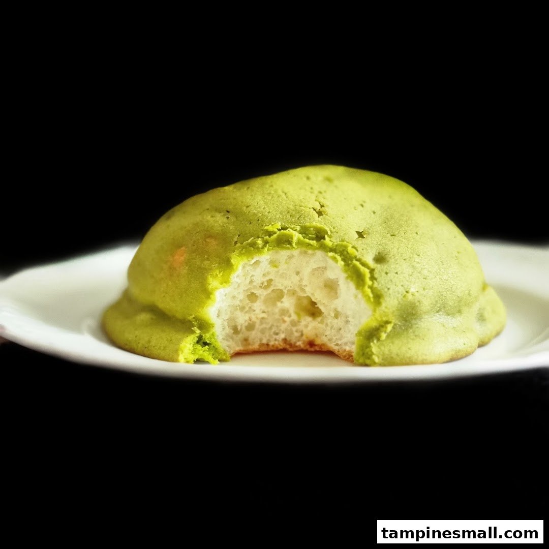 A vibrant green matcha melon pan, bitten to reveal its soft, fluffy interior, on a white plate.
