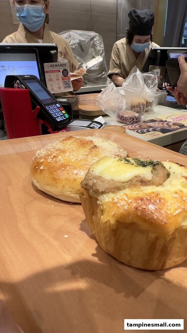 Freshly baked goods on a wooden tray at the Gokoku Japanese Bakery counter with staff in the background.