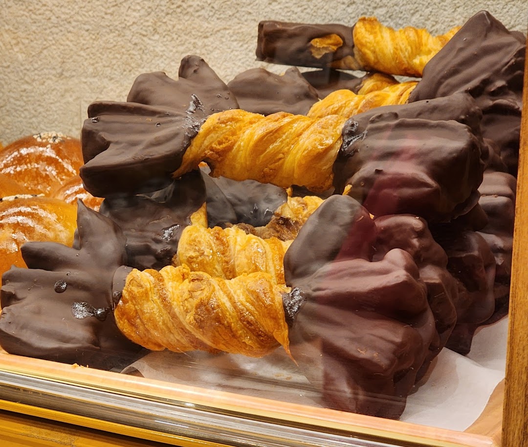 A close-up of chocolate-dipped pastries and golden twisted croissants displayed in a bakery case.