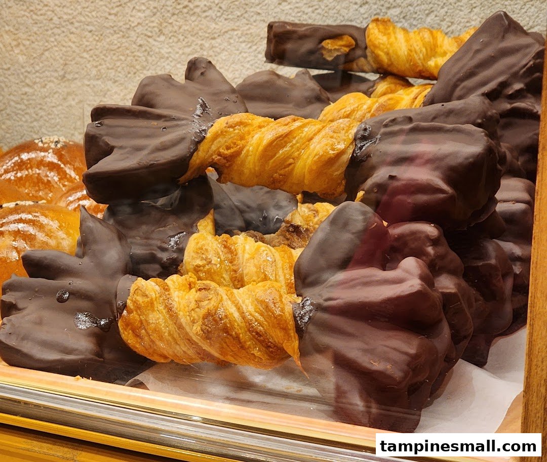 A close-up of chocolate-dipped pastries and golden twisted croissants displayed in a bakery case.