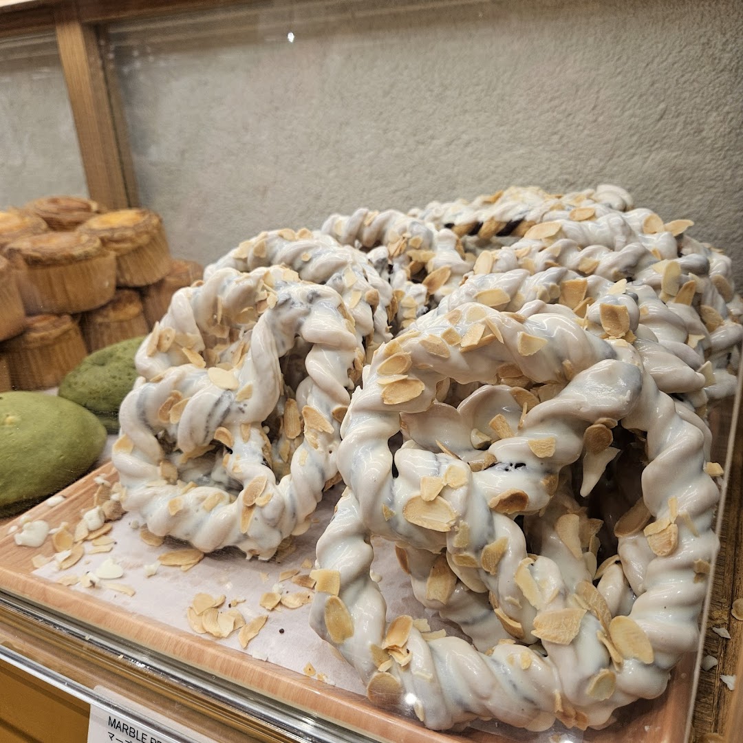 Close-up of white-glazed, almond-topped twisted pastries in a bakery display case.