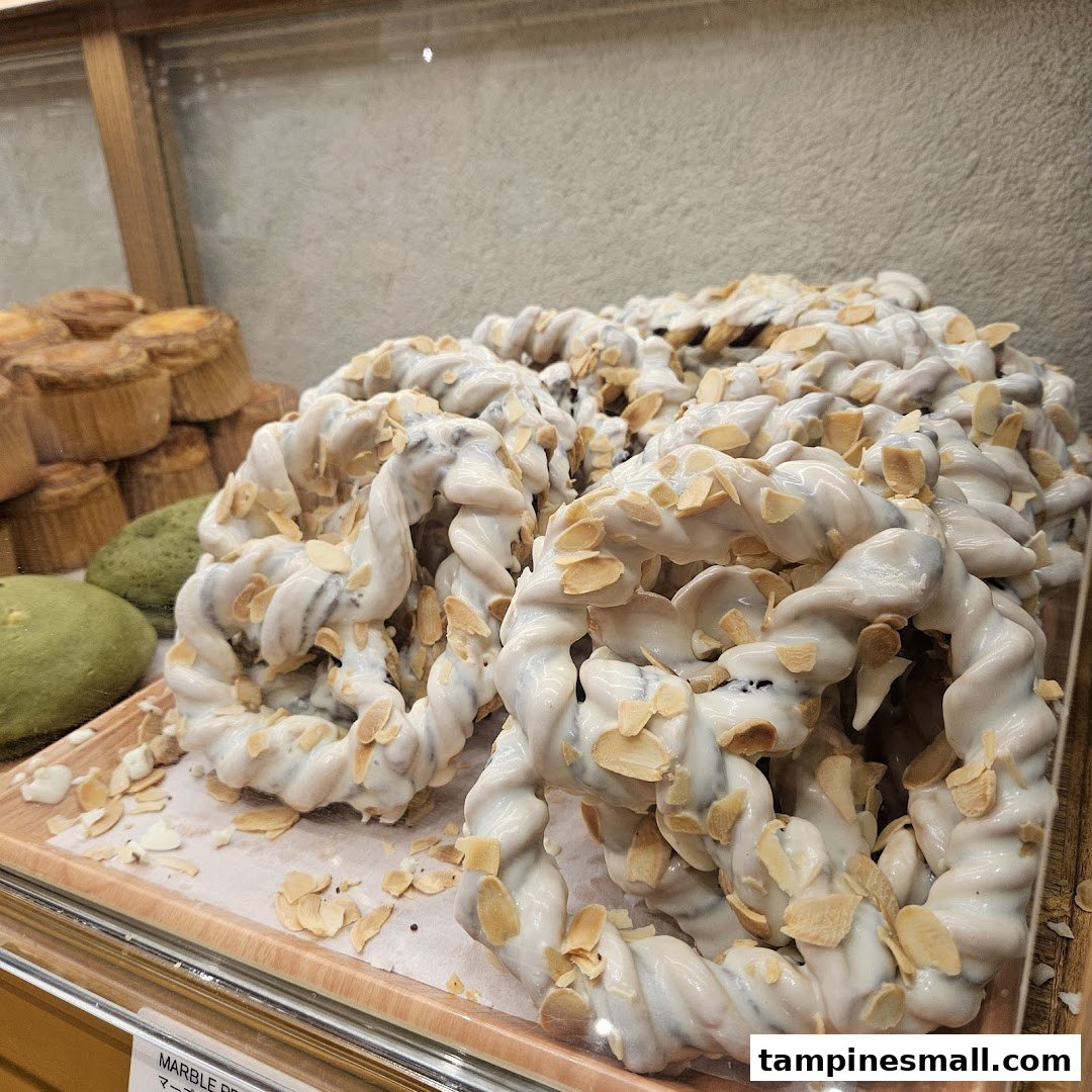 Close-up of white-glazed, almond-topped twisted pastries in a bakery display case.
