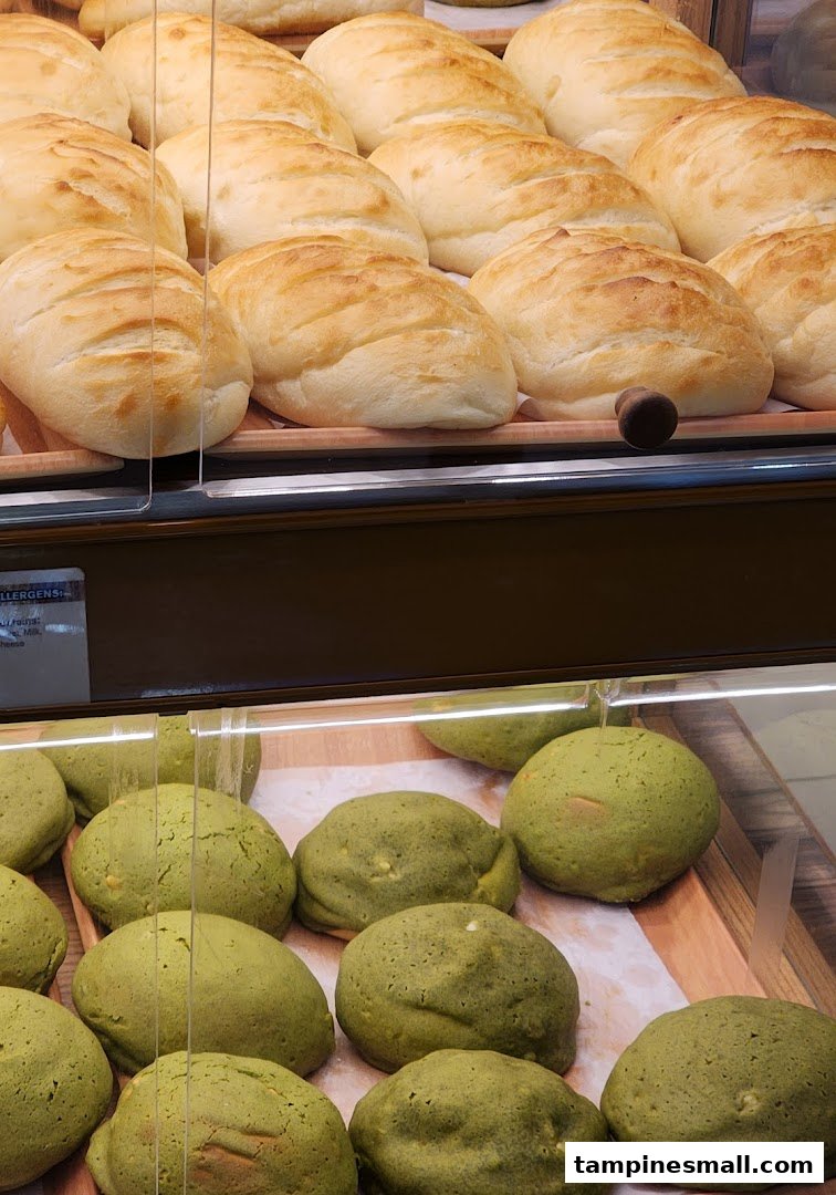 Close-up of freshly baked light-colored and green buns displayed in a bakery case.