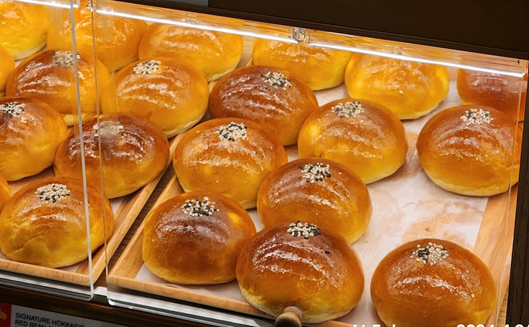 Rows of golden-brown buns with sesame seeds displayed in a bakery showcase.