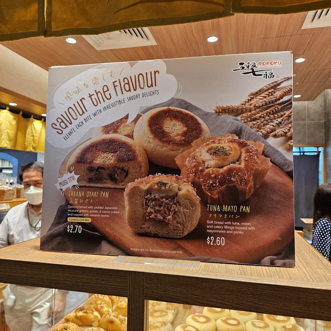 A promotional display board showcasing savory breads like Takana Oyaki Pan and Tuna Mayo Pan at Gokoku Japanese Bakery.