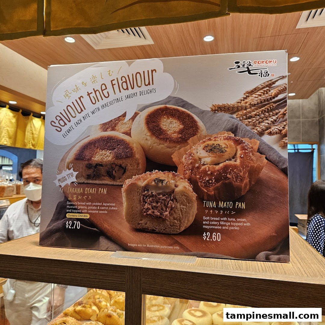 A promotional display board showcasing savory breads like Takana Oyaki Pan and Tuna Mayo Pan at Gokoku Japanese Bakery.