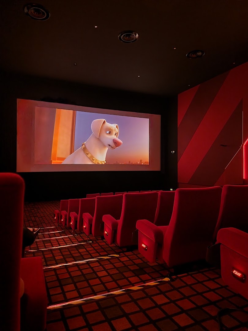 A cinema hall with comfortable red seats and a large screen displaying an animated movie.