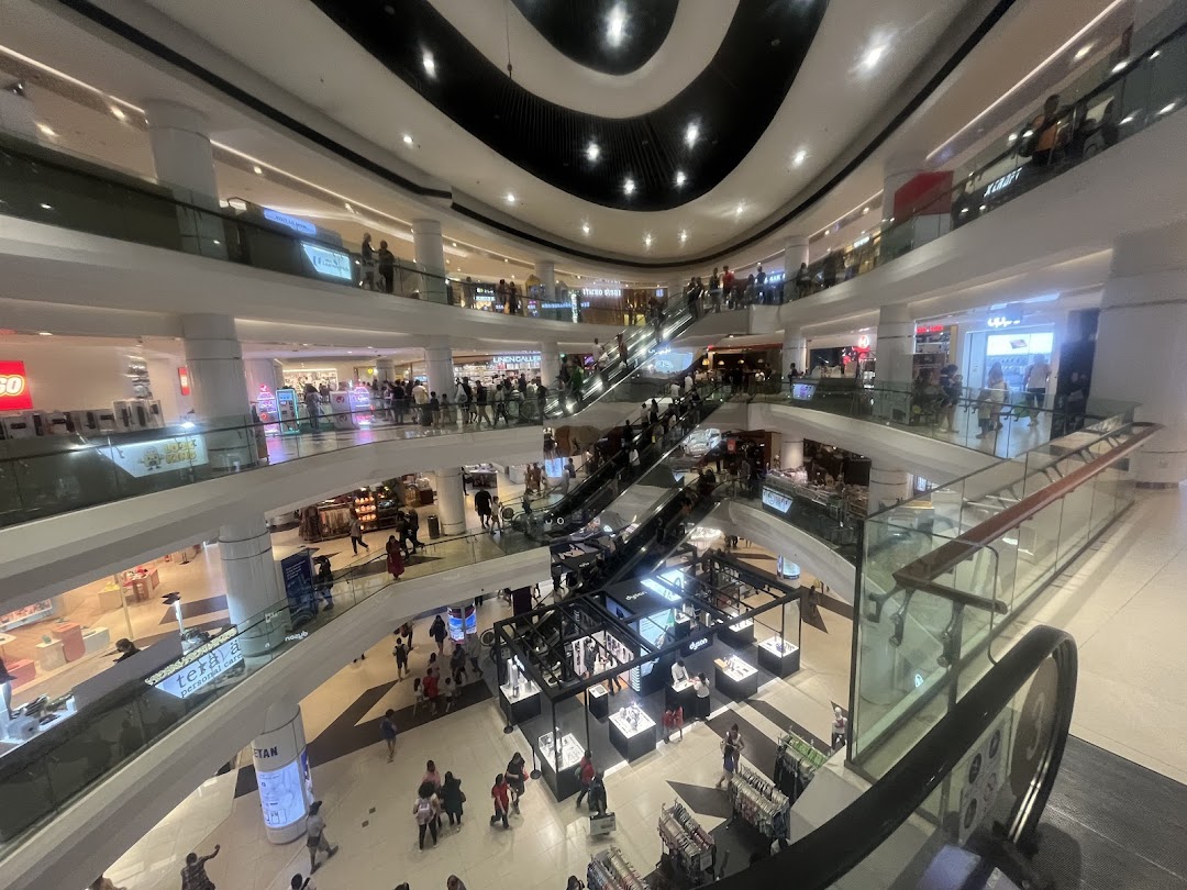 A bustling multi-level shopping mall interior with escalators, various shops, and many shoppers.
