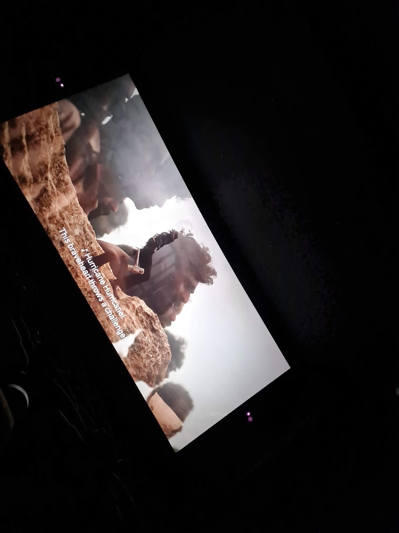 A movie scene with subtitles displayed on a large screen in a dark cinema hall.