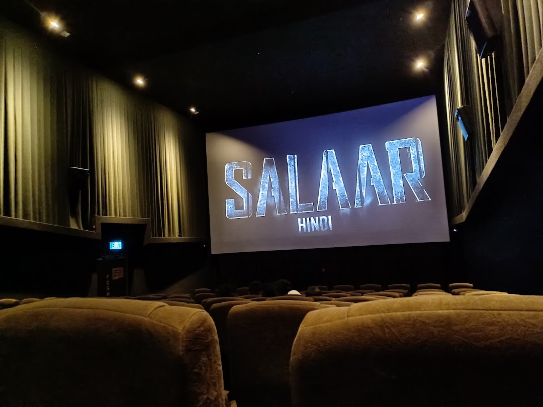 A cinema hall interior with plush seats and a large screen displaying 'SALAAR HINDI'.