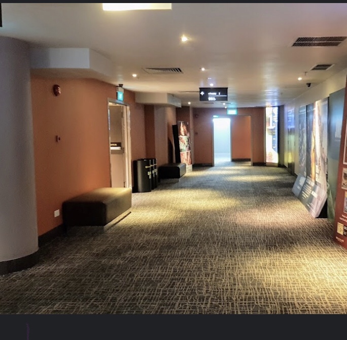 A spacious, carpeted cinema lobby with seating, directional signs, and movie posters.
