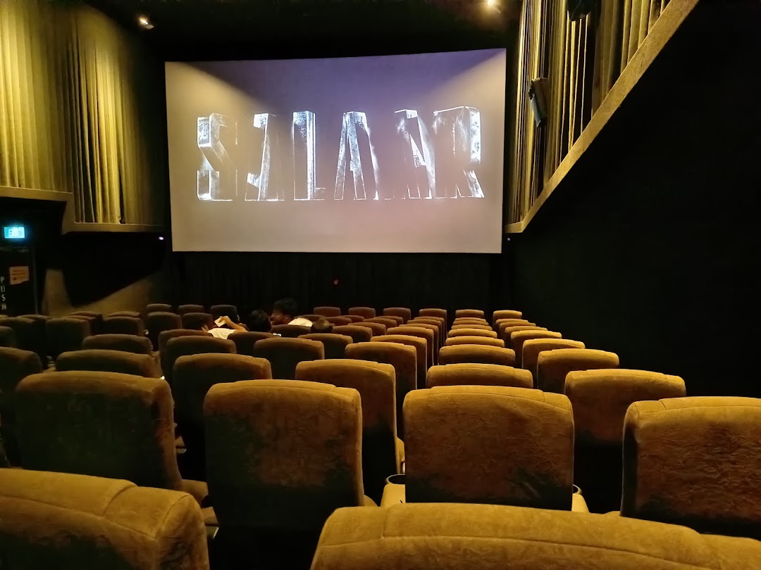 Interior view of a cinema hall with rows of seats and a large screen displaying text.