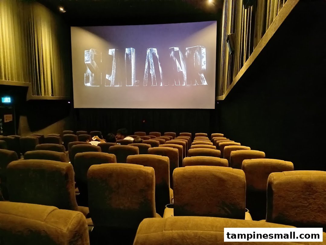 Interior view of a cinema hall with rows of seats and a large screen displaying text.
