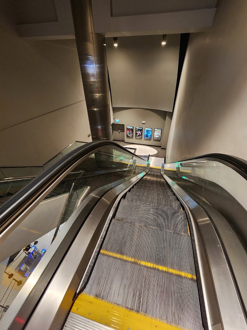 An escalator leading down to the Golden Village Tampines cinema lobby, featuring movie posters.