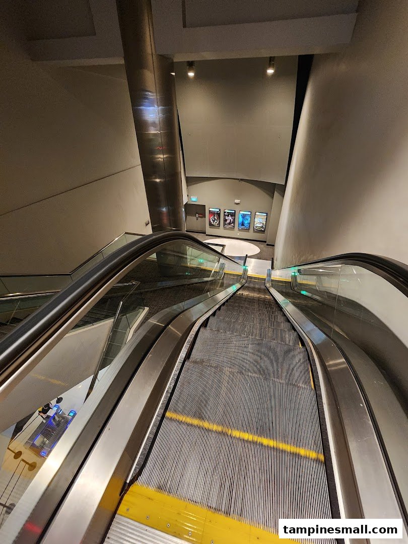 An escalator leading down to the Golden Village Tampines cinema lobby, featuring movie posters.