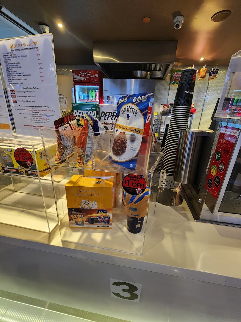 A cinema concession stand displaying snacks, drinks, and movie rating information at Golden Village Tampines.
