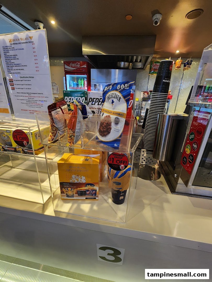 A cinema concession stand displaying snacks, drinks, and movie rating information at Golden Village Tampines.