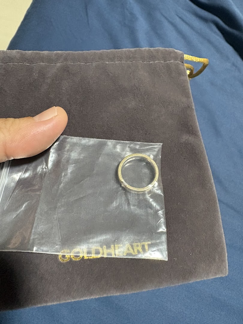 A Goldheart ring in clear plastic packaging, placed on a branded velvet pouch.