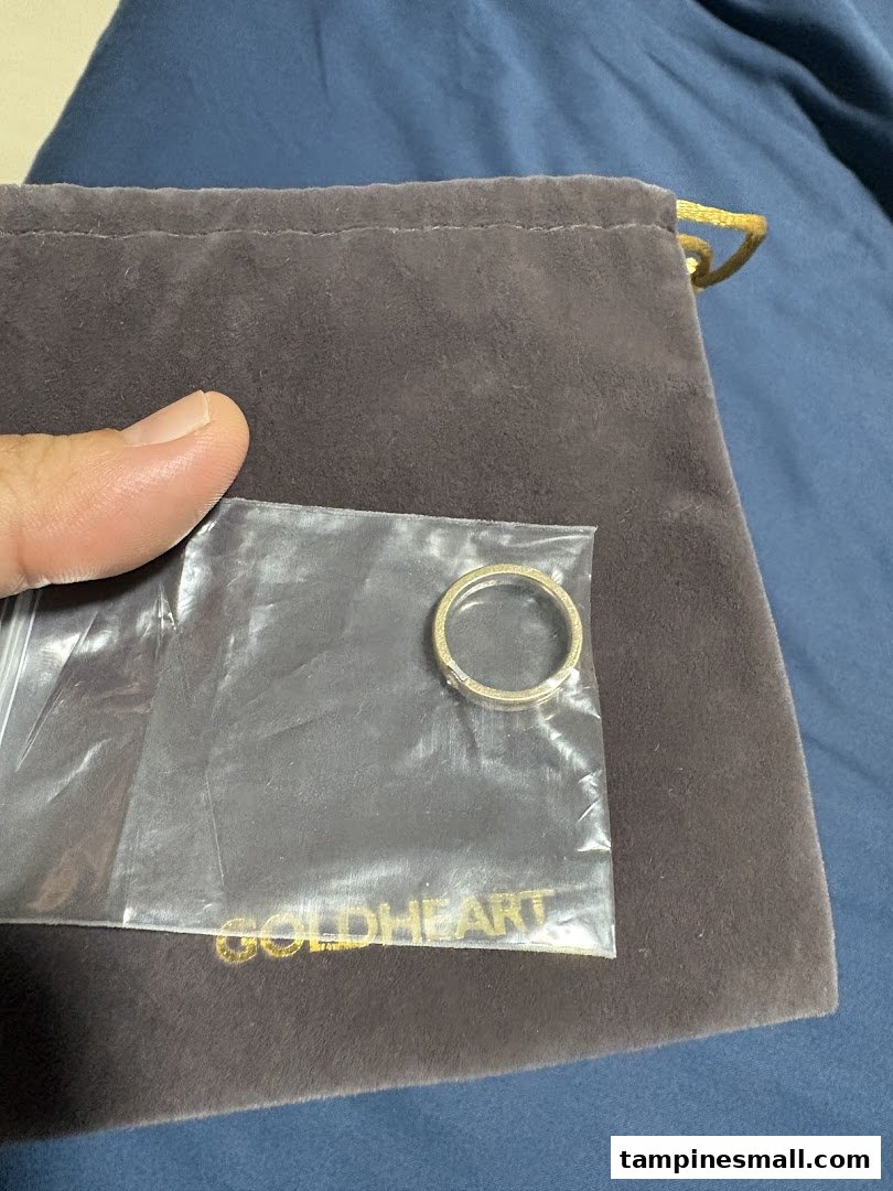 A Goldheart ring in clear plastic packaging, placed on a branded velvet pouch.
