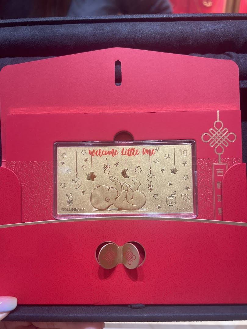 A Goldheart 'Welcome Little One' gold bar in a festive red gift box, perfect for celebrating new arrivals.