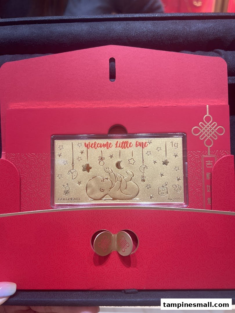 A Goldheart 'Welcome Little One' gold bar in a festive red gift box, perfect for celebrating new arrivals.