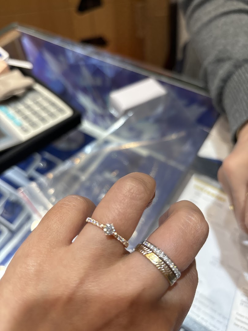 A hand models two elegant rings, a solitaire and a diamond band, at Goldheart Jewelry.