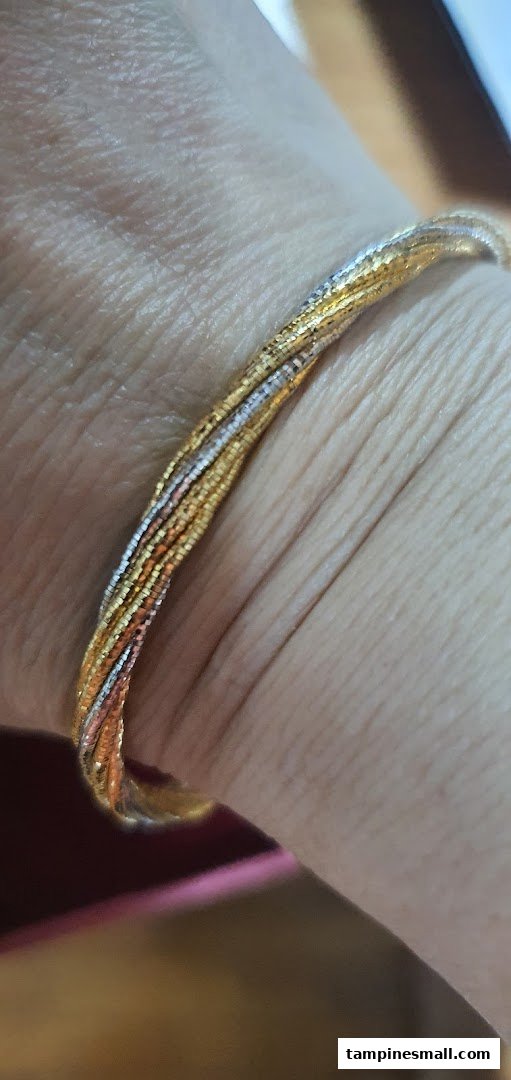 Close-up of a multi-tone gold bracelet with intricate design worn on a wrist.