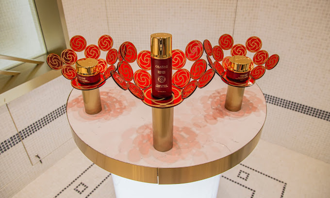 GRATiAE skincare products displayed on elegant stands with red and gold floral accents.