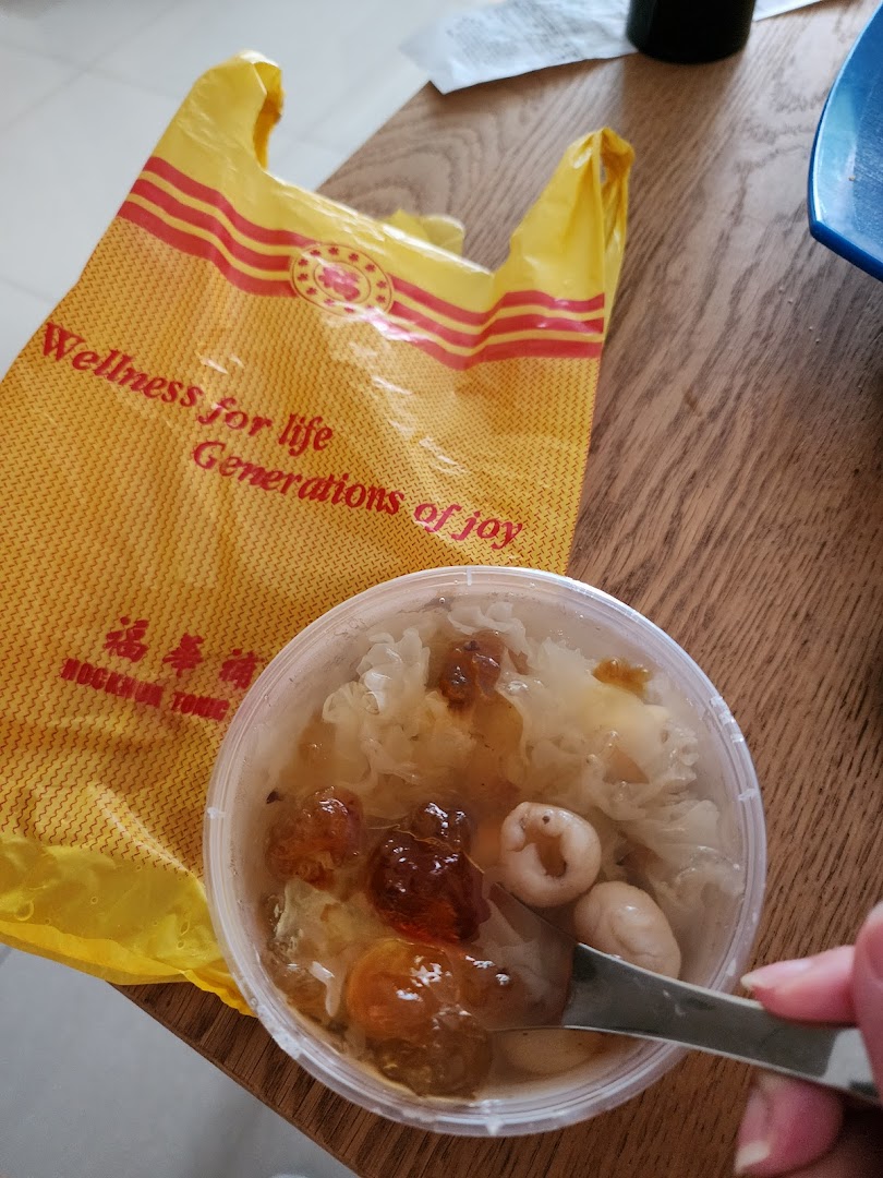 A clear container of traditional Chinese dessert/tonic with a spoon, next to a yellow Hockhua Tonic shopping bag.