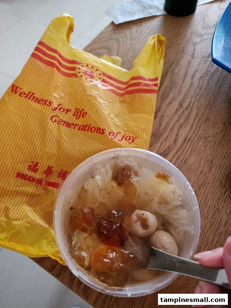 A clear container of traditional Chinese dessert/tonic with a spoon, next to a yellow Hockhua Tonic shopping bag.