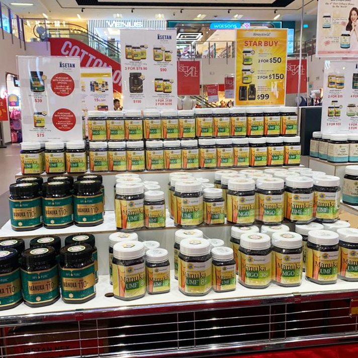 A retail display showcasing various Manuka honey products with promotional offers at HoneyWorld - Isetan Tampines.