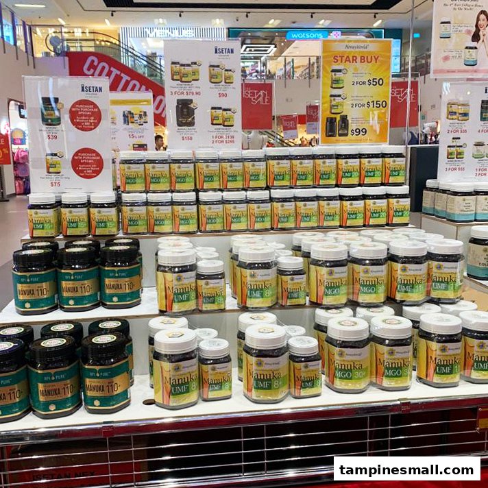 A retail display showcasing various Manuka honey products with promotional offers at HoneyWorld - Isetan Tampines.